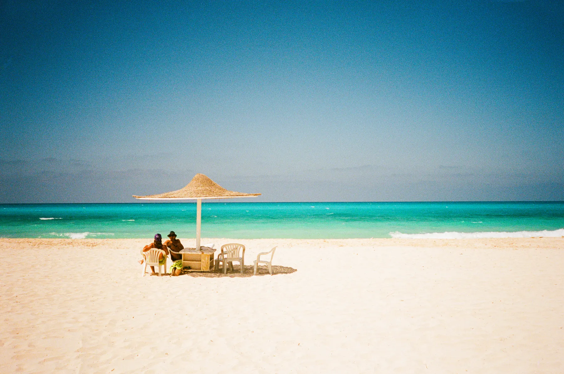 two people under a straw umbrella before a turquoise sea, marassi beach, egypt